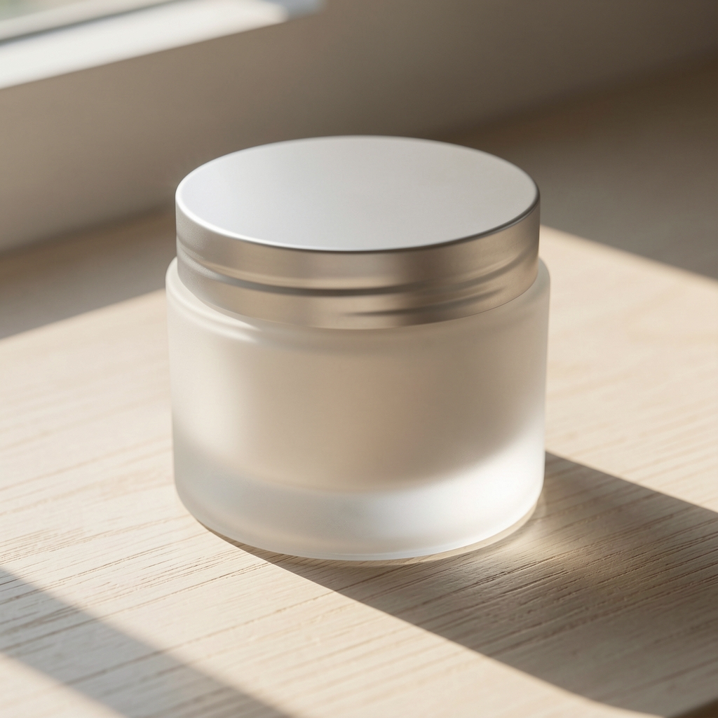 Wide frosted glass body moisturiser pot on a pale wooden surface, morning window light creating long gentle shadows across the product